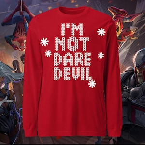 Peut inclure: Un t-shirt rouge à manches longues avec l'inscription "I'M NOT DARE DEVIL" en lettres blanches façon tricot. Des flocons de neige blancs ornent le texte. Vêtement festif sur le thème des fêtes.