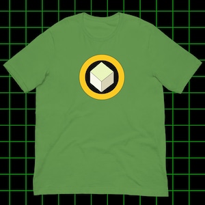 Peut inclure: T-shirt vert avec un motif de cube géométrique à l'intérieur d'un cercle jaune avec un contour noir. Le cube est vert clair et blanc. Le t-shirt est en matière souple.