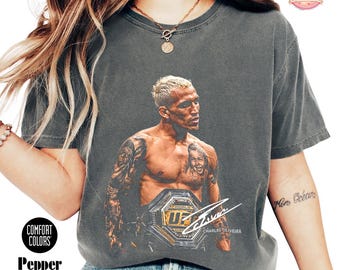 May include: A charcoal gray short-sleeve t-shirt featuring a graphic print of Charles Oliveira with a UFC championship belt. The design includes a white signature and the text Charles Oliveira. The shirt has a vintage wash and a crew neckline.