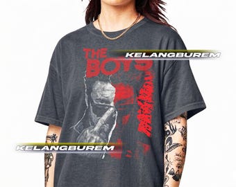 May include: Dark gray t-shirt featuring the text "THE BOYS" in red, along with a graphic of a person. The shirt has a vintage, distressed look.