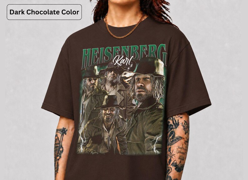 May include: Dark chocolate brown t-shirt with a graphic of a man and the text "HEISENBERG Karl" in green and white. The image shows the man in multiple poses, wearing a hat and jacket. The shirt has a crew neck.