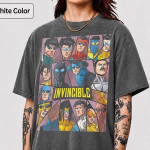 May include: A graphite-colored short-sleeve t-shirt featuring a graphic print of various characters from the Invincible series arranged in a grid. The word INVINCIBLE is printed in bold yellow capital letters across the center of the graphic.