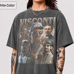 Pode incluir: Uma t-shirt de manga curta na cor grafite com uma estampa gráfica de cinco homens em várias poses, com o texto "VISCONTI" no topo e "Ace" num boné de basebol. A t-shirt tem gola redonda e um acabamento lavado de inspiração vintage.
