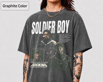 May include: A graphite-colored short-sleeve t-shirt featuring a graphic print of the character Soldier Boy. The design includes the text "SOLDIER BOY" at the top, "FUCKING UNPROFESSIONAL" at the bottom, and three distinct images of the character.