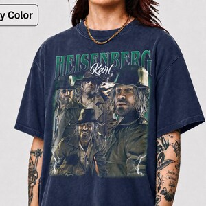 May include: Navy blue t-shirt with a graphic of men in hats and the text "HEISENBERG Karl" in green. The design has a vintage, distressed appearance.