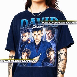 Puede incluir: Camiseta azul marino con un diseño de David Tennant en varias poses, con el nombre "DAVID" en azul arriba. La palabra "Tennant" está debajo. La camiseta tiene un estilo vintage y es una prenda clásica para fans.