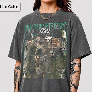 May include: Graphite grey t-shirt with a vintage graphic. The graphic features the text "HEISENBERG Karl" in green, and a group of men in hats and coats. The shirt has a worn appearance.
