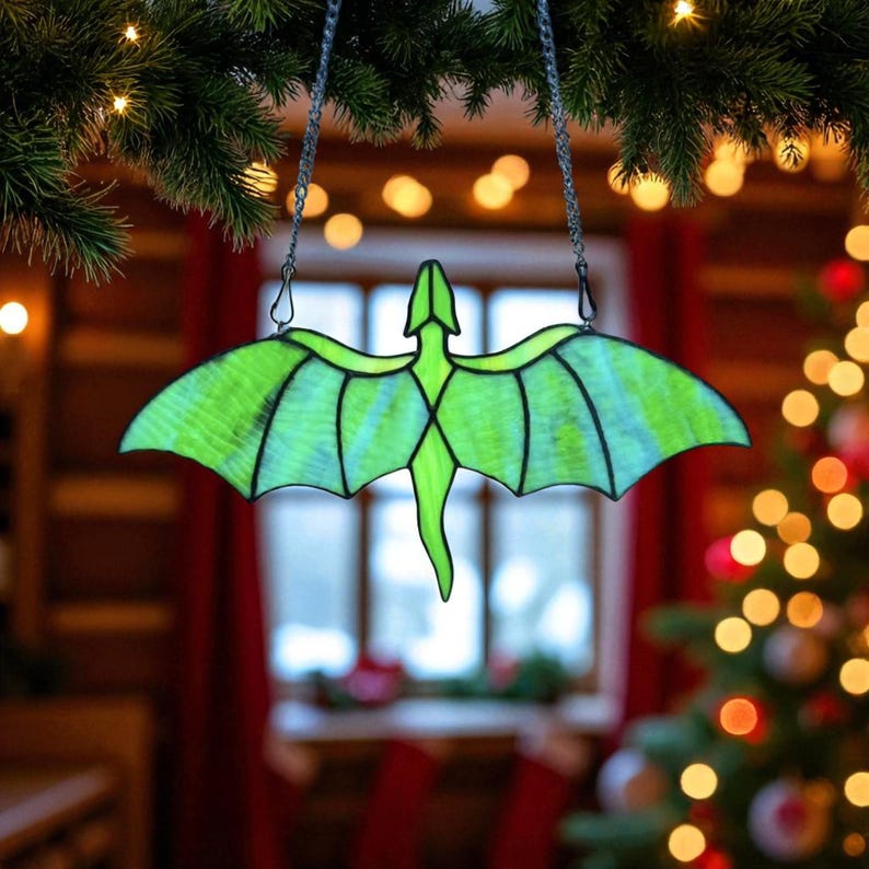 May include: A stained glass dragon ornament in shades of green and blue, hanging from a chain. The dragon has outstretched wings and a long tail. The background includes Christmas lights and a decorated tree.