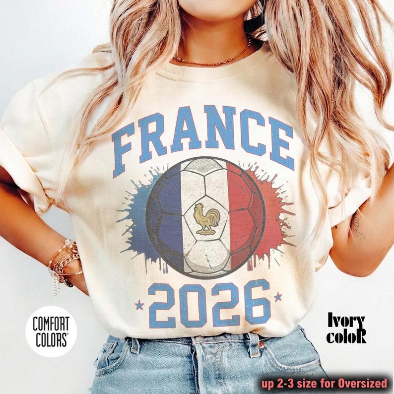 Op de afbeelding: Ivoor kleurige sweatshirt met het woord "FRANCE" in blauwe blokletters boven een voetbalontwerp in de kleuren van de Franse vlag. Het jaar "2026" is onder de bal gedrukt. Het shirt is van Comfort Colors.