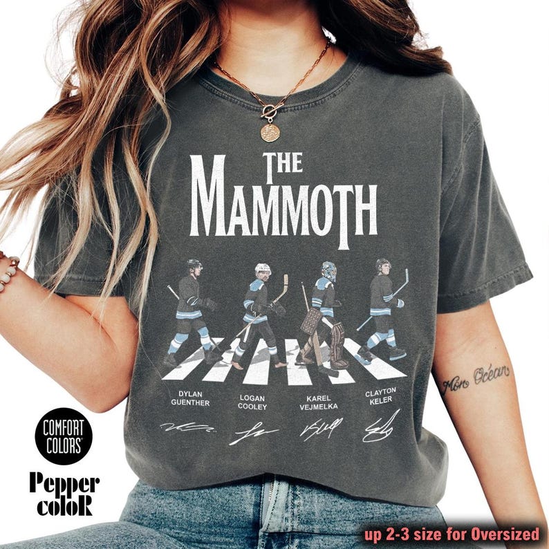 K&ouml;nnte beinhalten: Dunkelgraues T-Shirt mit dem Text "The Mammoth" &uuml;ber einer Illustration von vier Eishockeyspielern, die einen Zebrastreifen &uuml;berqueren. Die Namen der Spieler sind unter der Illustration aufgedruckt. Das Shirt tr&auml;gt auch die Aufschrift "Comfort Colors" und "Pepper color".