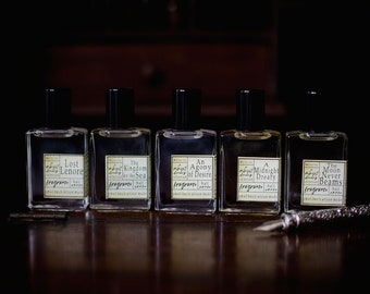 Puede incluir: Cinco pequeños frascos de perfume de vidrio con tapas negras y etiquetas. Las etiquetas son de color crema con texto negro y enumeran los nombres de los perfumes: Lost Lenore, The Kingdom by the Sea, An Agony of Desire, A Midnight Dreary y The Moon Never Beams.