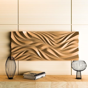 May include: A wooden wall art piece with a wave-like design, mounted above a wooden surface. Two black metal decorative objects and a stack of books are on the surface. The wall behind the art is light-coloured wood panelling.