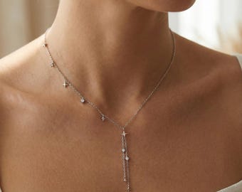 Peut inclure: Un délicat collier argenté orné de petits pendentifs en forme d'étoiles et de ronds. Le collier a un design en forme de Y avec des breloques pendantes. Le collier est porté autour du cou.