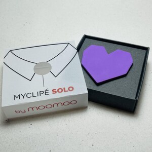 May include: A purple heart-shaped accessory rests in a black box next to a white box with a shirt collar illustration. The white box has the text "MYCLIP&Eacute; SOLO" and "by moomoo" printed on it.