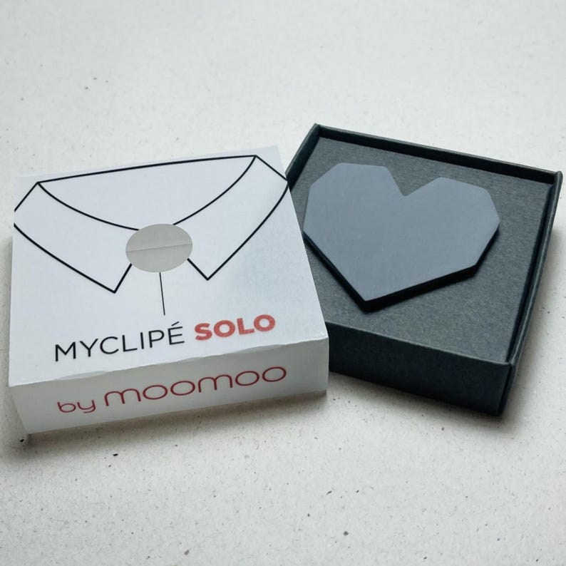 May include: A white box with a black collar illustration and the text "MYCLIP&Eacute; SOLO by moomoo" next to a gray heart-shaped object in a dark gray box. The heart is a geometric design.