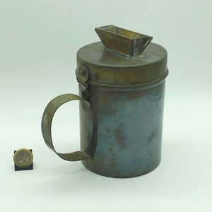 May include: A brass container with a spout and a handle. The container has a worn, aged look.