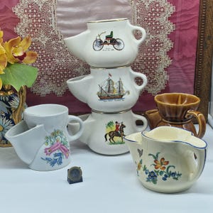 Puede incluir: Colección de tazas de afeitar vintage. Las tazas de porcelana blanca presentan varios diseños, incluyendo una bicicleta, un velero y un jinete a caballo. Algunas tazas tienen diseños florales y ribetes dorados.