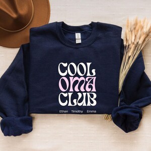 May include: Navy blue sweatshirt with the text "Cool Oma Club" in white and pink lettering. The names Ethan, Timothy, and Emma are printed below the text.