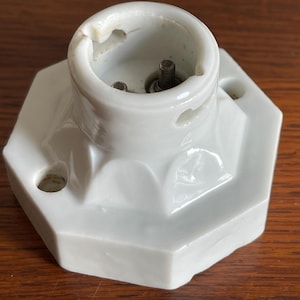 Peut inclure: Un luminaire en porcelaine blanche avec une base hexagonale et une seule douille. La douille a deux broches métalliques.