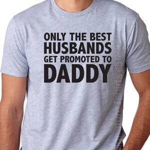 May include: A gray t-shirt with the text "Only the best husbands get promoted to Daddy" printed in black.