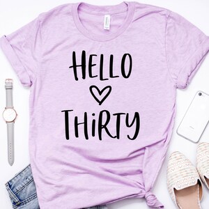 May include: A lavender t-shirt with the text "HELLO THIRTY" in black lettering with a heart symbol between the words.