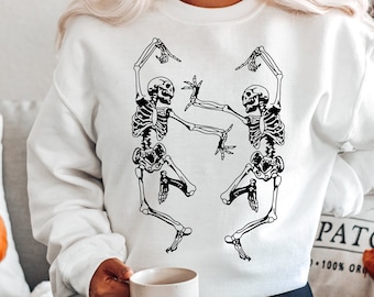 May include: White sweatshirt with a black graphic of two skeletons dancing. The skeletons are in a playful pose with their arms raised.