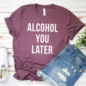 Pu&ograve; includere: Una maglietta color marsala con la scritta "ALCOHOL YOU LATER" in lettere bianche.