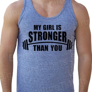 May include: A heather gray tank top with a black graphic that says "My girl is stronger than you" with a barbell graphic above the text.