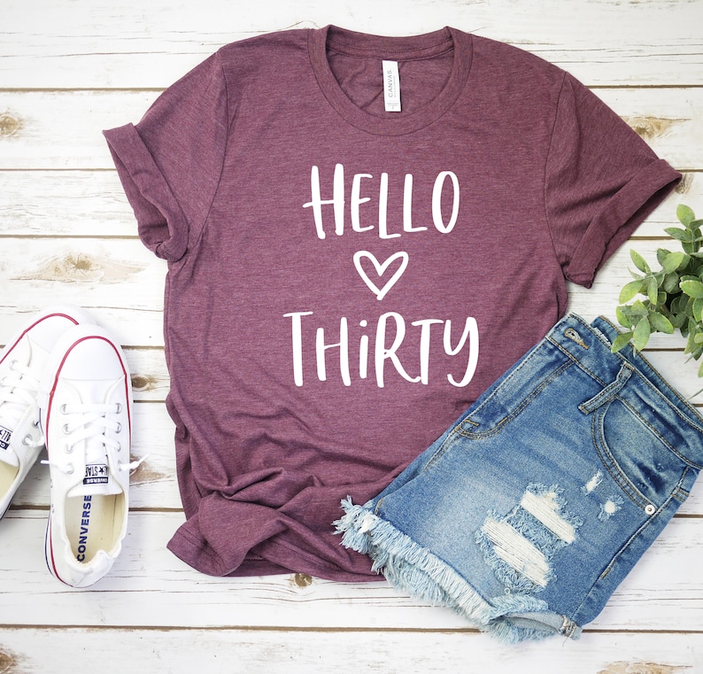 May include: A maroon t-shirt with the text "Hello Thirty" in white with a white heart between the words.