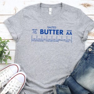 May include: Gray t-shirt with blue text that reads "Salted Butter Grade AA" and a graphic of a stick of butter with measurements in tablespoons and cups.
