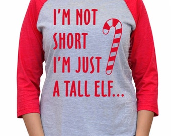 May include: A gray and red baseball tee shirt with the text "I'm not short I'm just a tall elf..." and a candy cane graphic.