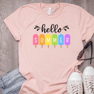 May include: A pink t-shirt with the text "hello summer" in black lettering. The text is surrounded by rainbow popsicle graphics.
