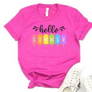 May include: Pink t-shirt with the text "hello summer" in black lettering. The word "summer" is spelled out with colorful popsicle graphics.