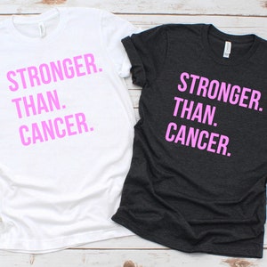 May include: Two t-shirts with the text "Stronger Than Cancer" printed in pink on the front. One t-shirt is white and the other is dark grey.