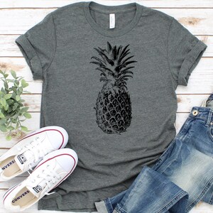 Pode incluir: Uma camiseta cinza mescla com um gr&aacute;fico de abacaxi preto e branco.