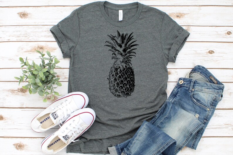 Pode incluir: Uma camiseta cinza mescla com um gr&aacute;fico de abacaxi preto e branco.