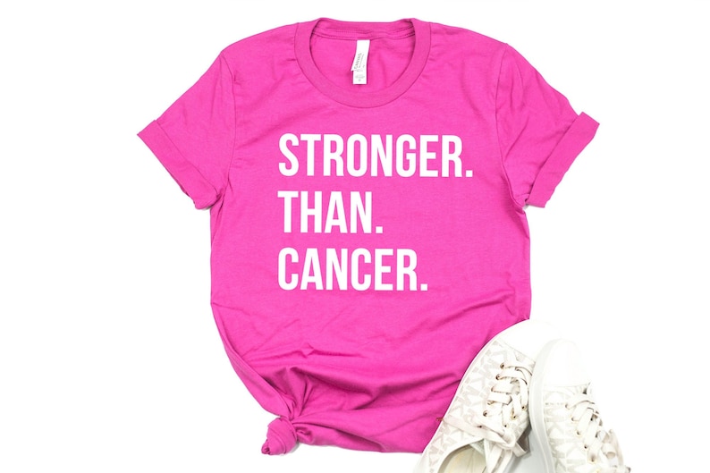 May include: Pink t-shirt with the text "STRONGER. THAN. CANCER." in white lettering.