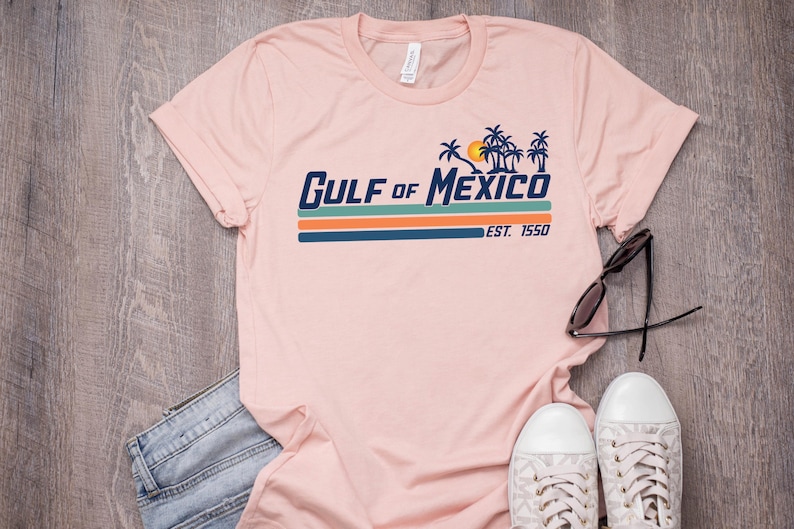 May include: A pink t-shirt with a retro-style graphic that says "GULF of MEXICO EST. 1950" with palm trees and a sun.