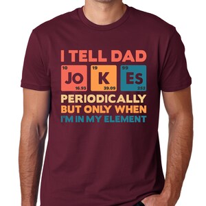 Puede incluir: Camiseta granate con el texto "I TELL DAD JOKES PERIODICALLY BUT ONLY WHEN I'M IN MY ELEMENT" en un dise&ntilde;o colorido de tabla peri&oacute;dica. La camiseta es de cuello redondo.