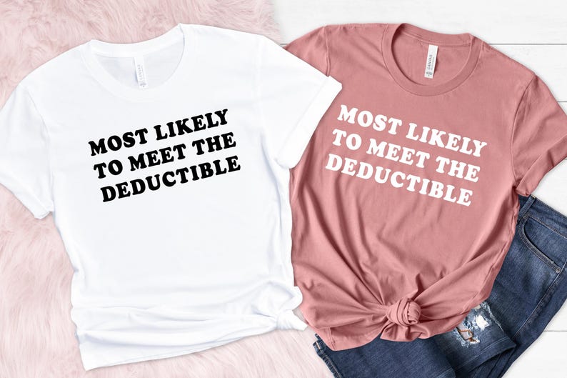 May include: Two t-shirts, one white and one dusty rose, with the text "MOST LIKELY TO MEET THE DEDUCTIBLE" in bold, black and white font. The white shirt is on the left, and the dusty rose shirt is on the right, with a pair of blue jeans.