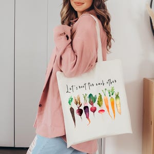 May include: White canvas tote bag with the text "Let's root for each other" and a watercolor illustration of various vegetables, including carrots, radishes, and beets.