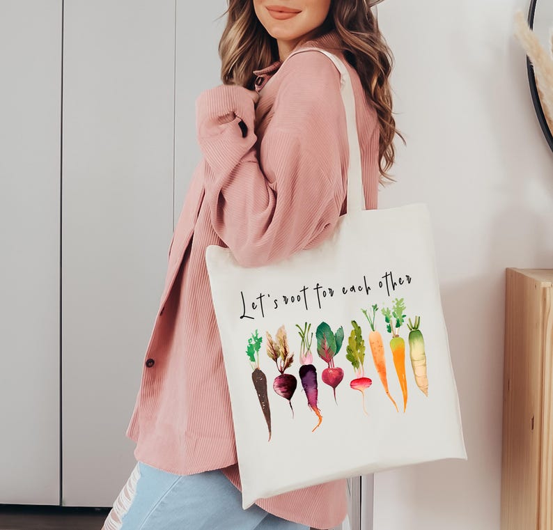 May include: White canvas tote bag with the text "Let's root for each other" and a watercolor illustration of various vegetables, including carrots, radishes, and beets.