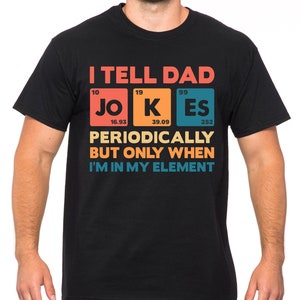 Puede incluir: Camiseta negra con el texto "I TELL DAD JOKES PERIODICALLY BUT ONLY WHEN I'M IN MY ELEMENT." El texto est&aacute; en un dise&ntilde;o colorido, con la palabra "JOKES" estilizada como elementos de la tabla peri&oacute;dica.