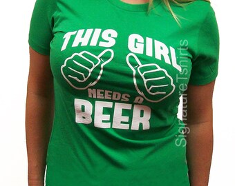 May include: Green t-shirt with white text that reads "This Girl Needs a Beer" with two thumbs up symbols.