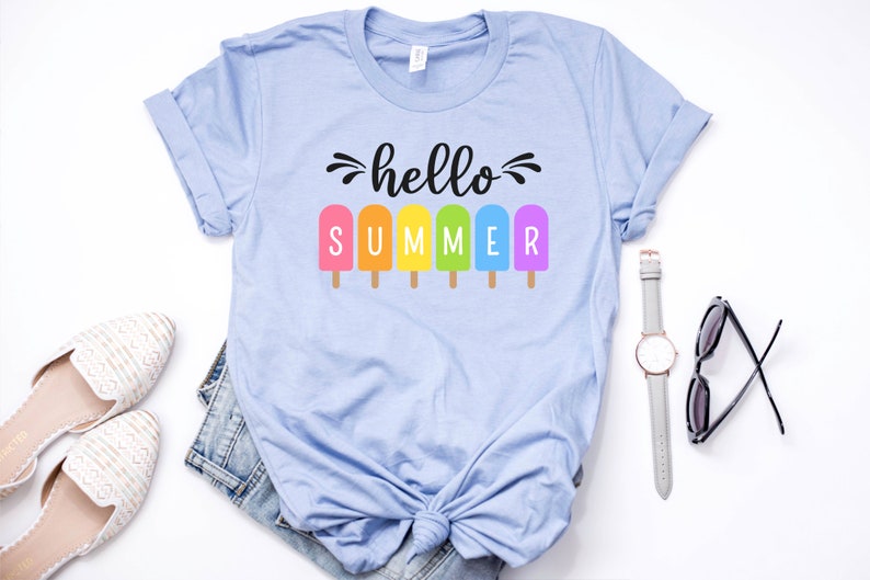 May include: A light blue t-shirt with the text "hello summer" in black script.  The text is surrounded by six rainbow popsicle graphics.