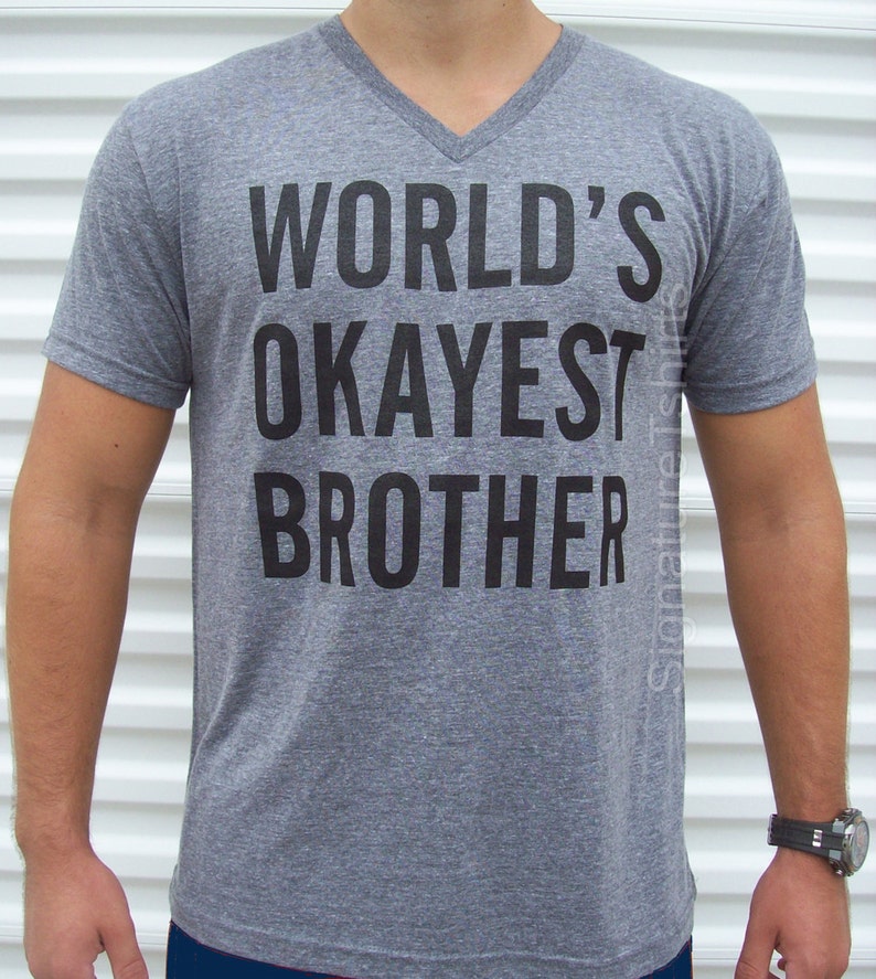 May include: Gray V-neck t-shirt with the text "WORLD'S OKAYEST BROTHER" printed in black.