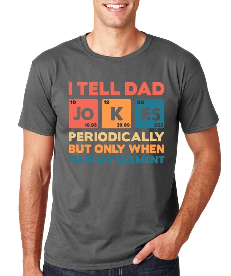 Puede incluir: Camiseta gris oscuro con la frase "I TELL DAD JOKES PERIODICALLY BUT ONLY WHEN I'M IN MY ELEMENT" en un dise&ntilde;o de tabla peri&oacute;dica. La camiseta tiene cuello redondo y mangas cortas.