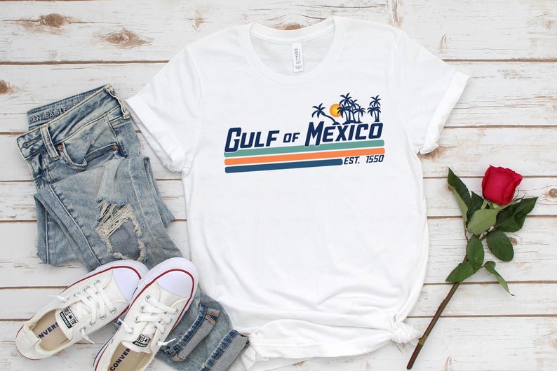 May include: White t-shirt with a blue and orange graphic that says "GULF of MEXICO EST. 1550". The graphic features palm trees and a sun.