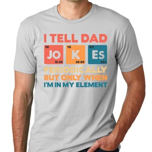 Puede incluir: Una camiseta gris claro con el texto "I TELL DAD JOKES PERIODICALLY BUT ONLY WHEN I'M IN MY ELEMENT" en rojo, naranja y azul. El texto est&aacute; dispuesto en un estilo de tabla peri&oacute;dica.