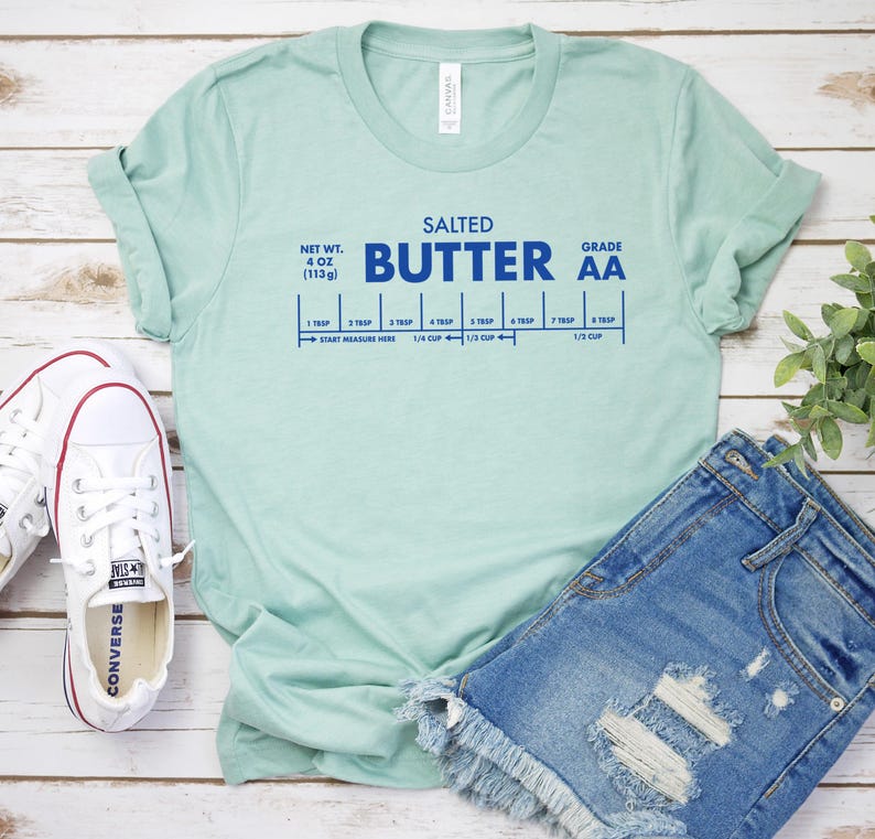 May include: A light blue t-shirt with the text "SALTED BUTTER AA" in blue lettering. The shirt also includes a graphic of a butter stick with measurements in tablespoons and cups.
